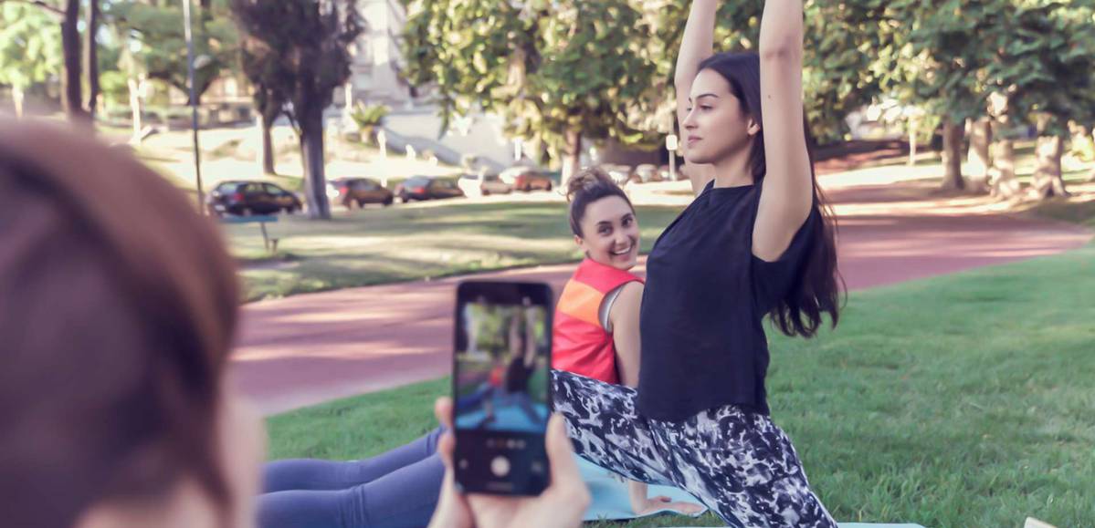 mulheres sentadas em um parque fazem poses de yoga e posam para a câmera de um celular